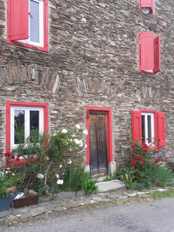 a stone building with red windows and a door at Au Grand Mûrier in Roquefère