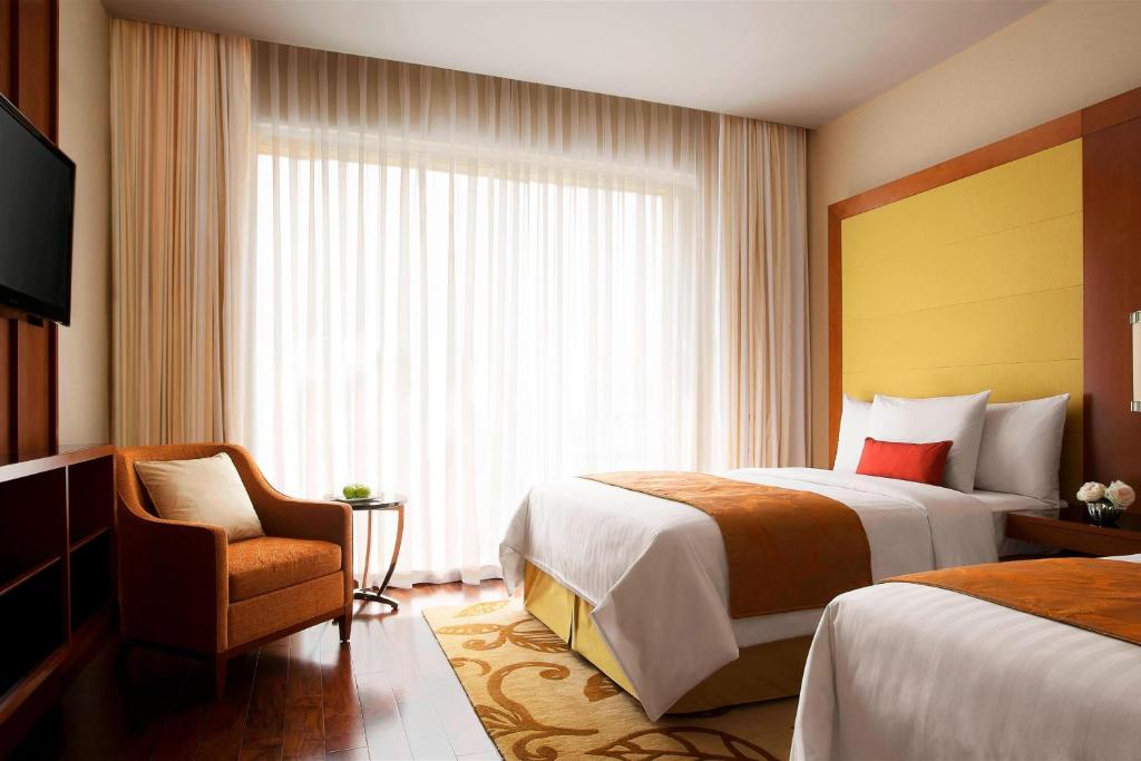 a hotel room with two beds and a chair and a window at Courtyard by Marriott Kochi Airport in Nedumbassery