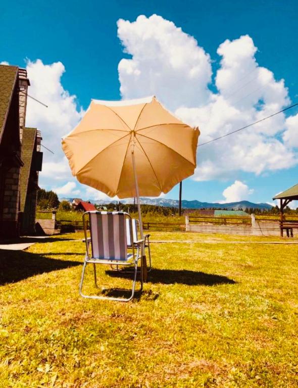 a chair with an umbrella sitting in the grass at Lulu Cottage in Žabljak
