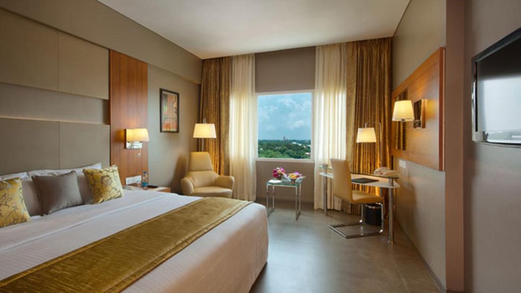a hotel room with a bed and a desk and a window at Royal Orchid Central Vadodara in Vadodara