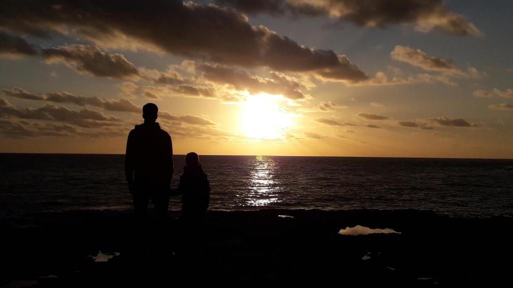 un homme et un enfant debout sur la plage regardant le coucher du soleil dans l'établissement Studio Le Charentais - logement de vacances 4 personnes bord de mer, à Vaux-sur-Mer