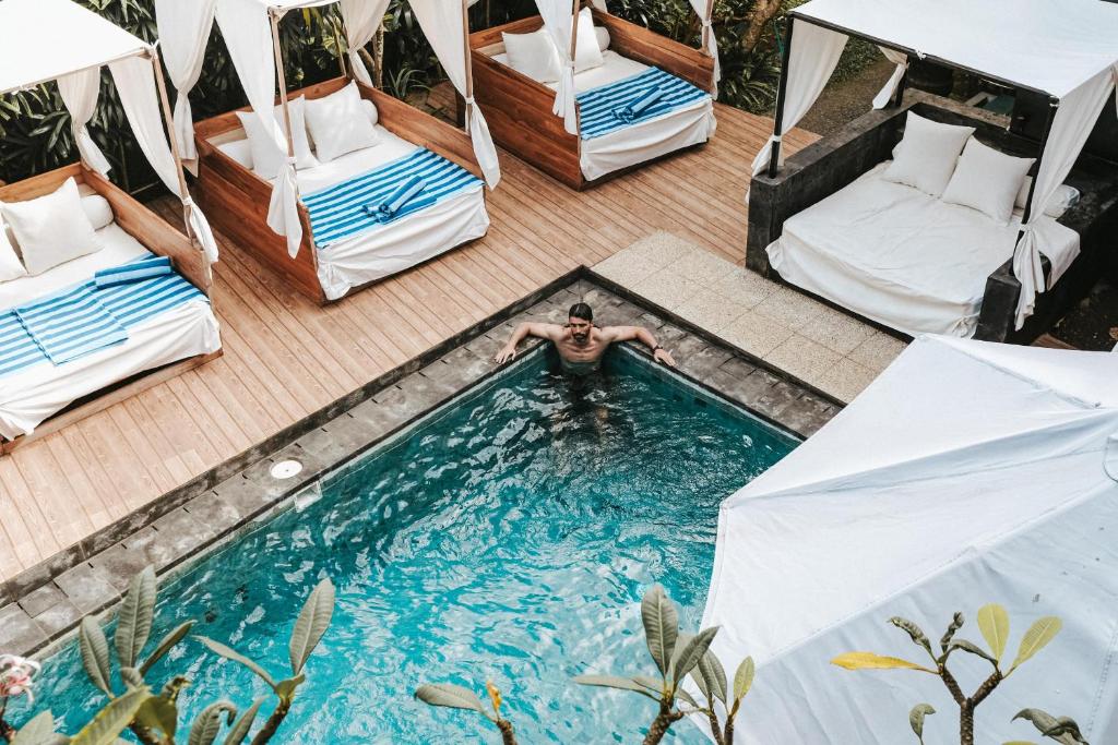 a man swimming in a pool with beds and tents at De Olas Padang Padang Bali in Uluwatu