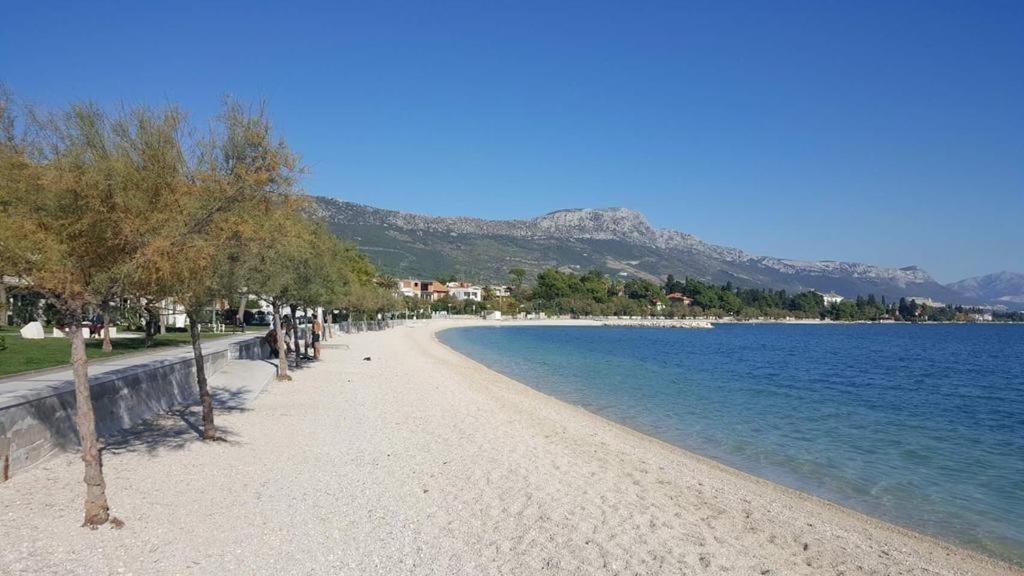 a beach with trees and the water on a sunny day at Apartmani Žaneta in Kaštela