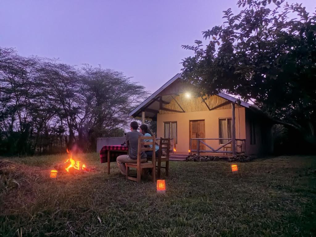two people sitting around a fire in front of a house at Nguse River Camp in Kikube