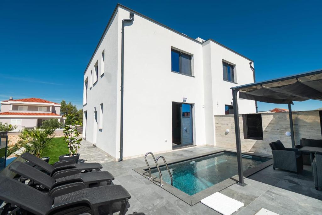 a white house with a swimming pool and chairs at Holiday house MAYA in Srima