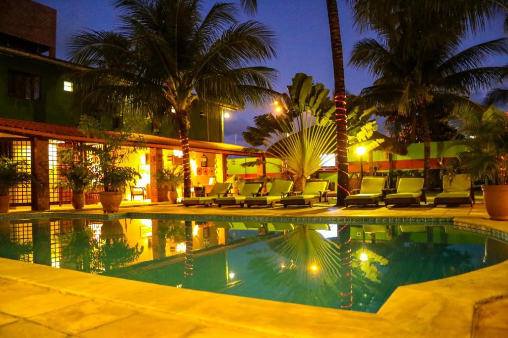 a resort pool with chairs and palm trees at night at Pousada Porto e Mar in Porto De Galinhas