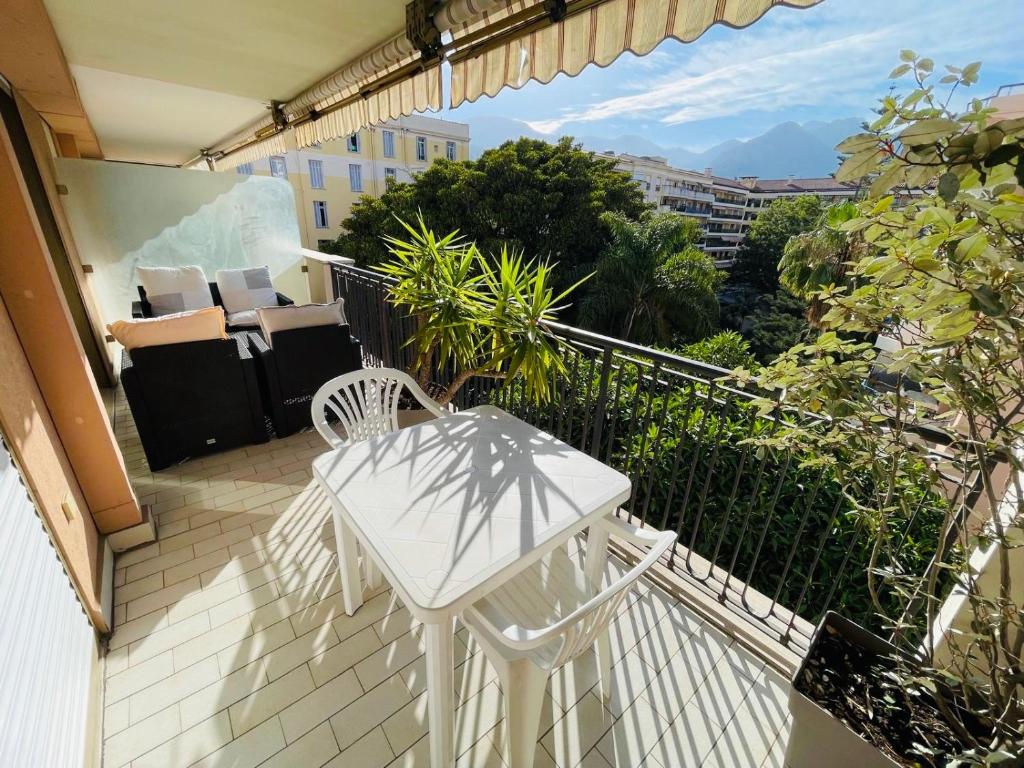 Elle comprend un balcon doté d'une table et de chaises blanches. dans l'établissement Beach apartment with tropical garden and mountain view Best location, à Menton