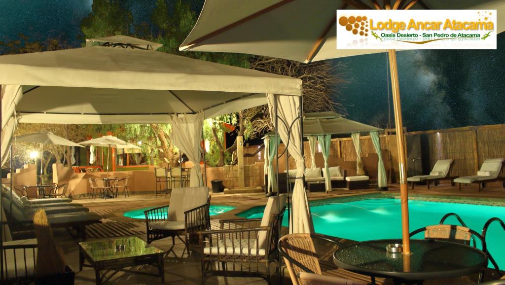 a swimming pool with chairs and tables and an umbrella at Lodge Ancar Atacama in San Pedro de Atacama