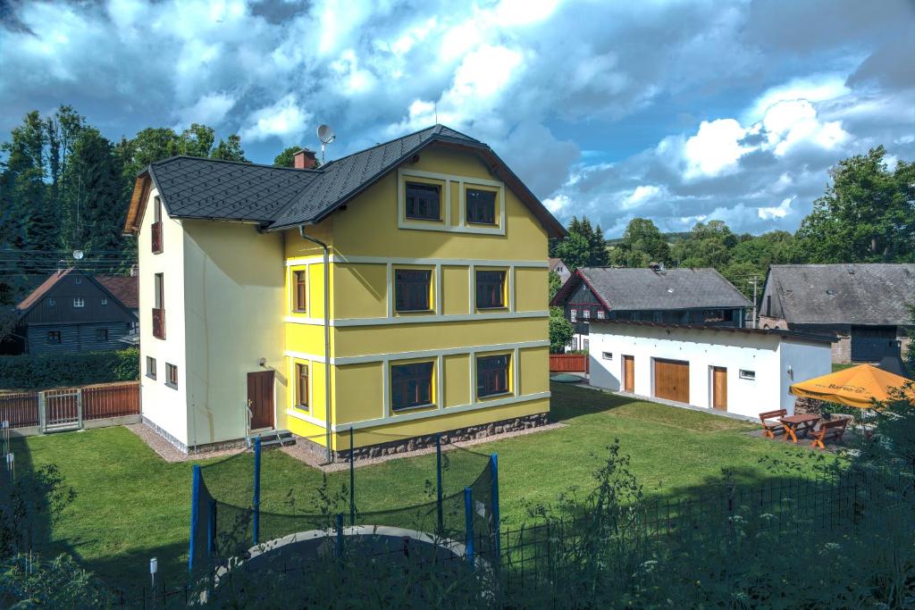 een geel huis met een zwart dak op een erf bij Apartmány Barto21 in Bartošovice v Orlických Horách