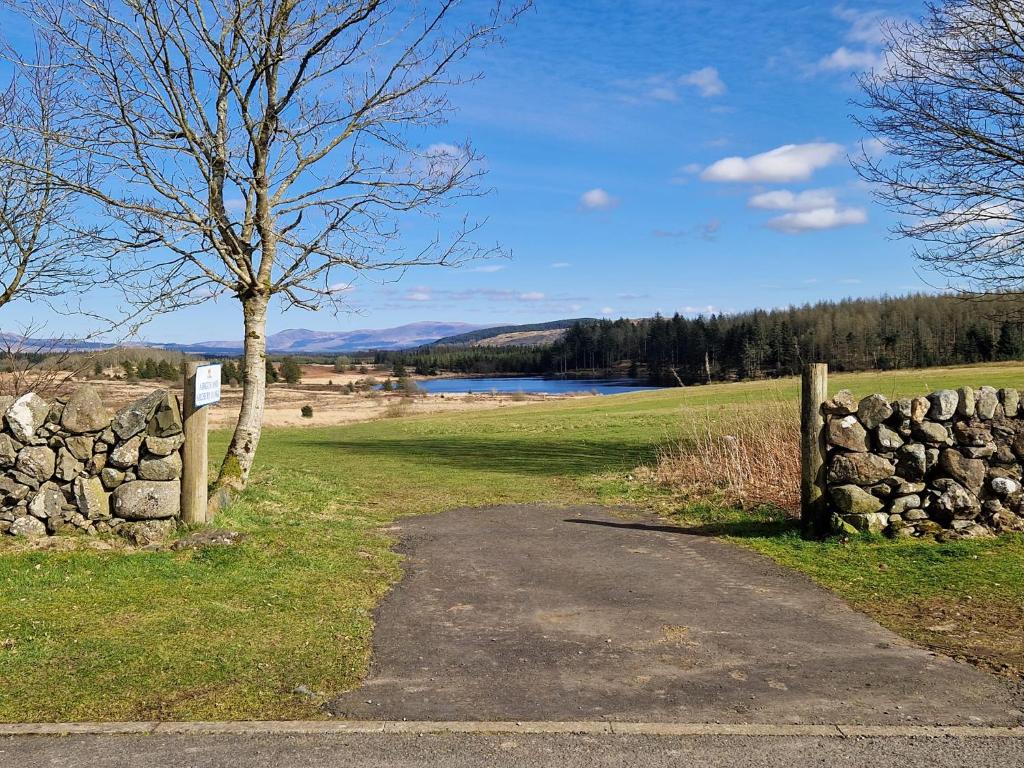 a stone fence and a tree next to a road at Lochview Retreat Caravan in Balminnoch