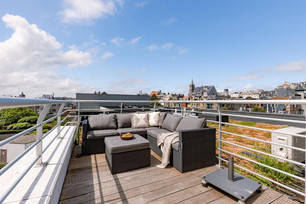 a balcony with a couch and a table on a roof at Huswell - Cozy seaside apartment with sunny terrace in Blankenberge
