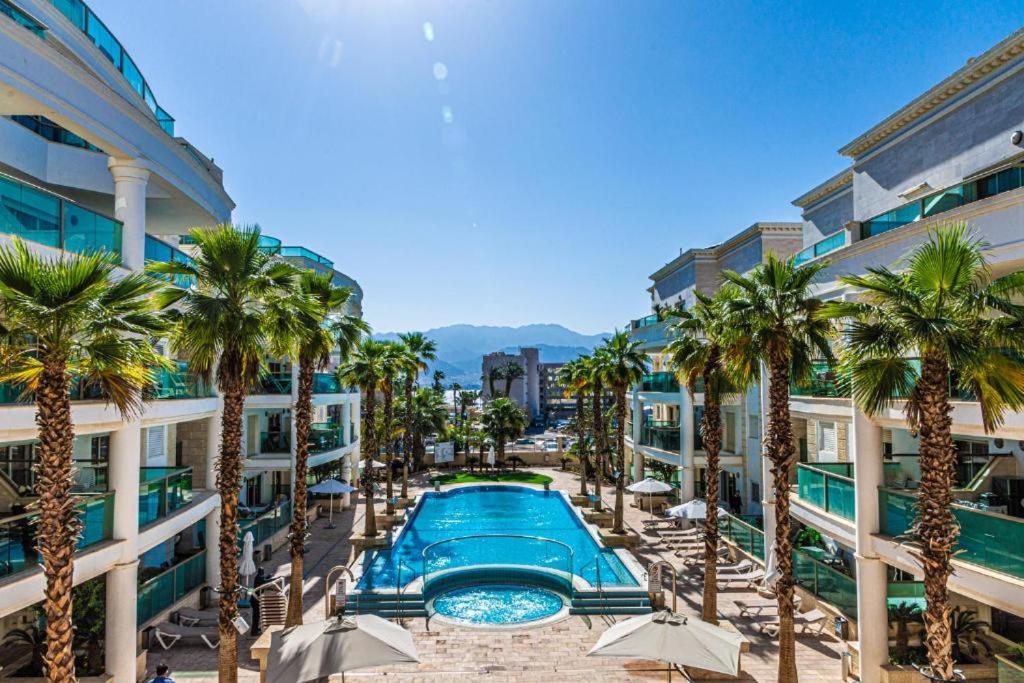 a swimming pool with palm trees in front of a building at מיני סוויטה לה פלמורה in Eilat