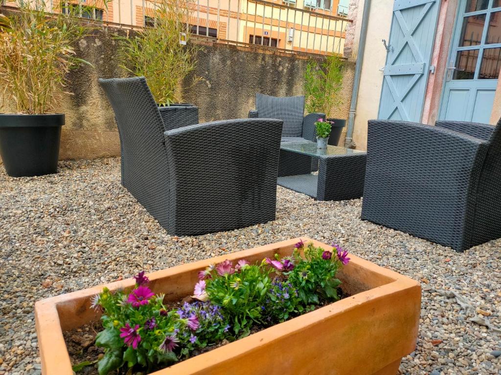 a patio with wicker chairs and a planter with flowers at Idéal famille & couple in Moissac