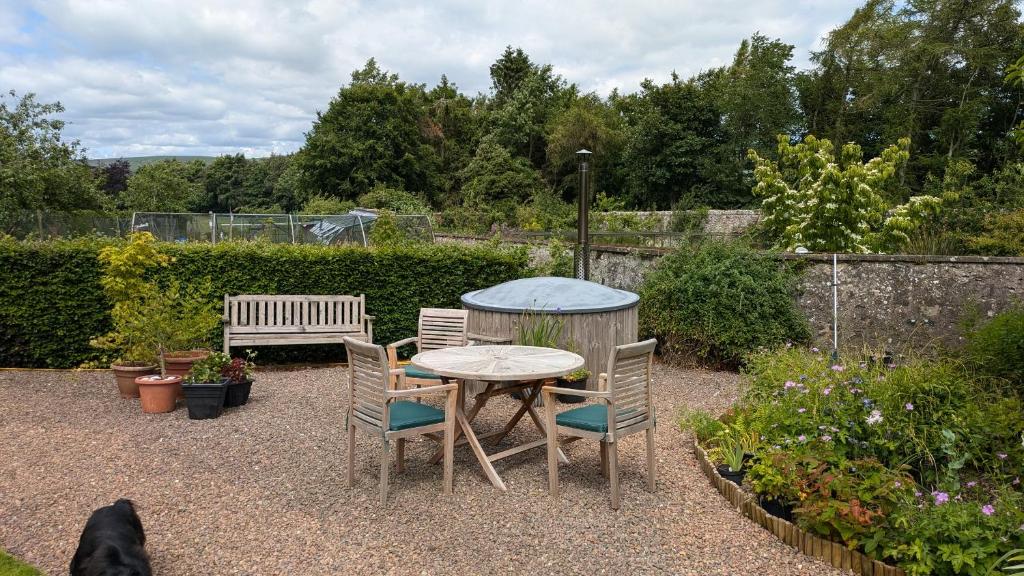 a table and chairs in a garden with a dog at Cumledge Yew Trees Cottage in Duns