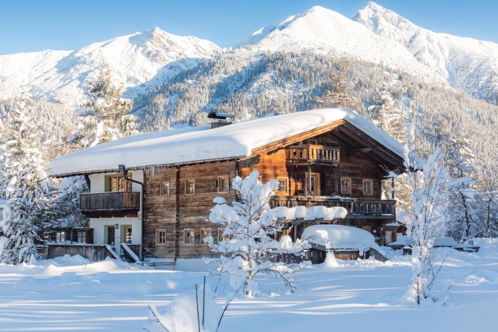 a log cabin in the snow with snow covered mountains at Bichlhof Appartements, mit Wellness im Hotel Charlotte in Seefeld in Tirol