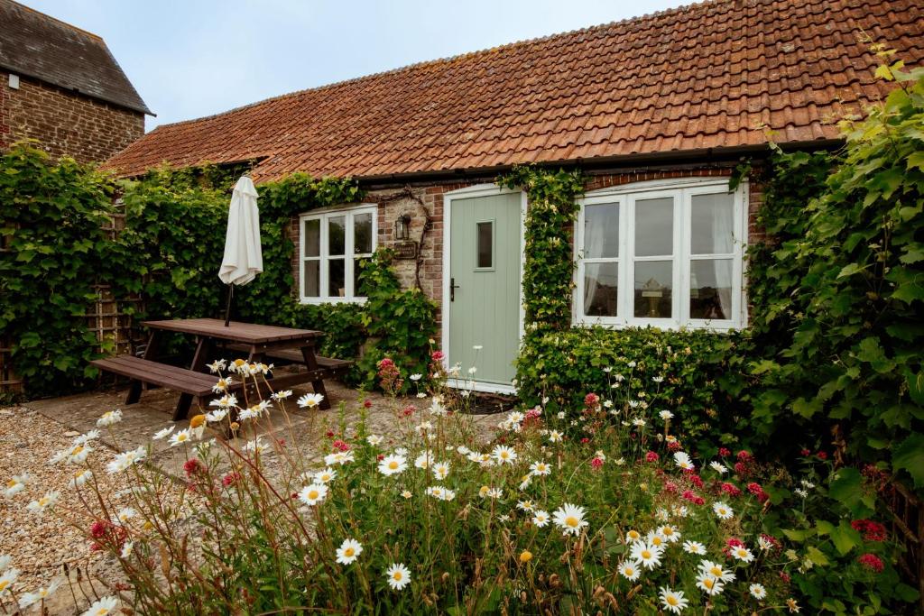a cottage with a bench and an umbrella and flowers at Milkmaids Cottage - Rudge Farm Cottages in Bridport