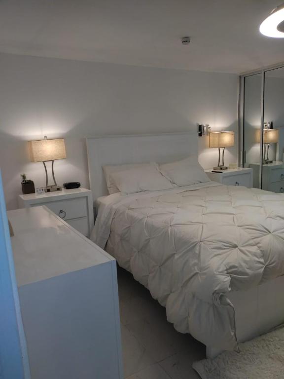 a white bedroom with a bed and two lamps at Luxury Apt for 4 Comfy Quiet AC & WiFi in San Felipe de Puerto Plata