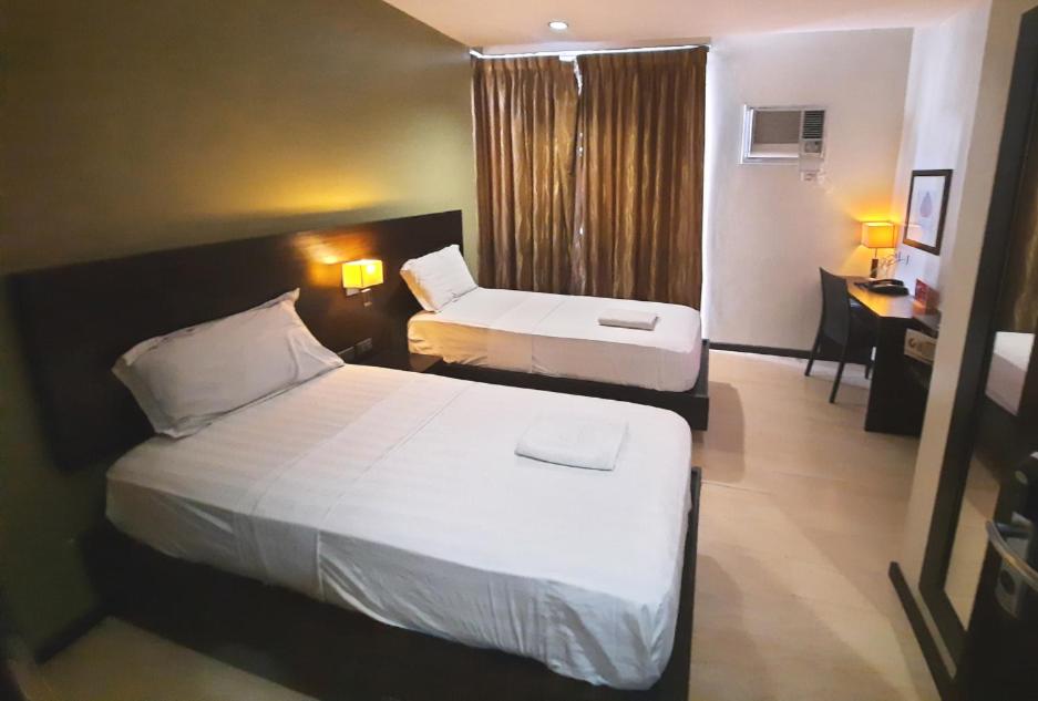 a hotel room with two beds and a desk at Lorenzzo Suites Hotel Makati in Manila