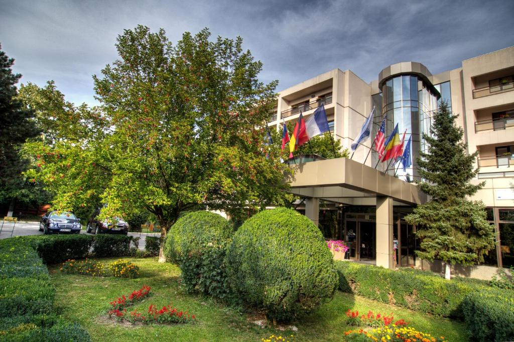 a building with bushes and flowers in front of a building at Hotel Dumbrava in Bacău