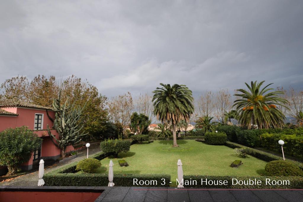 a garden with palm trees and a pink house at Solar de Lalém in Maia