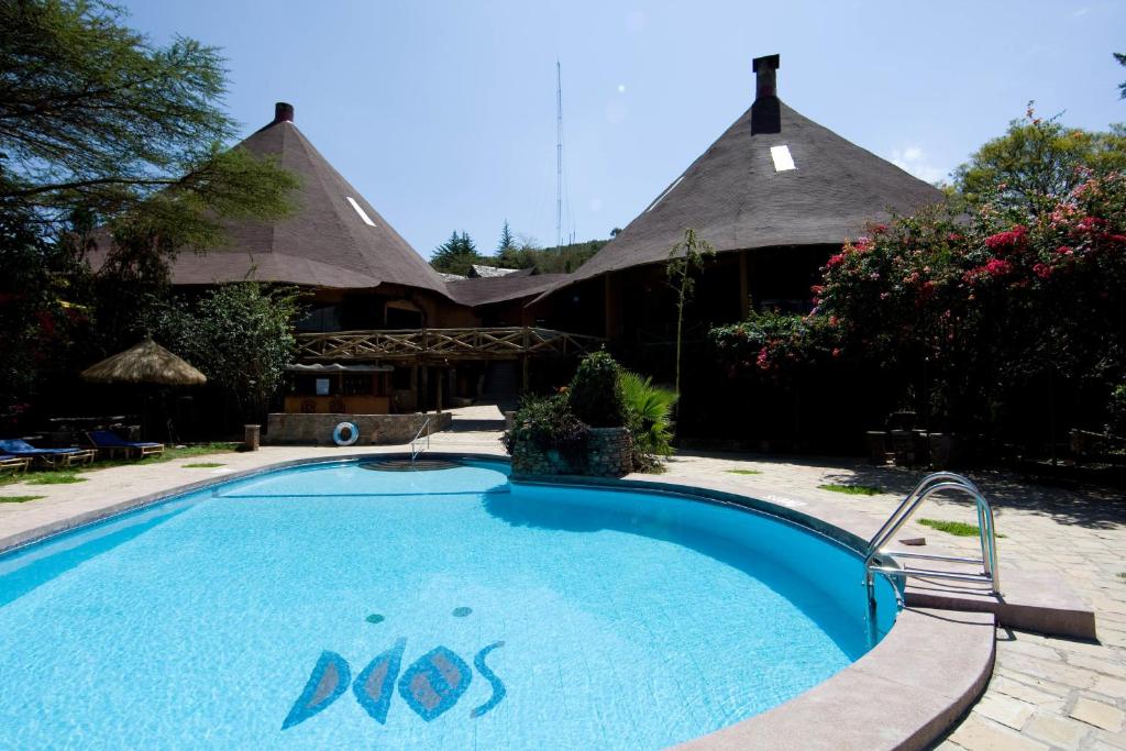 a swimming pool with a house with a thatch roof at Masai Mara Sopa Lodge in Ololaimutiek