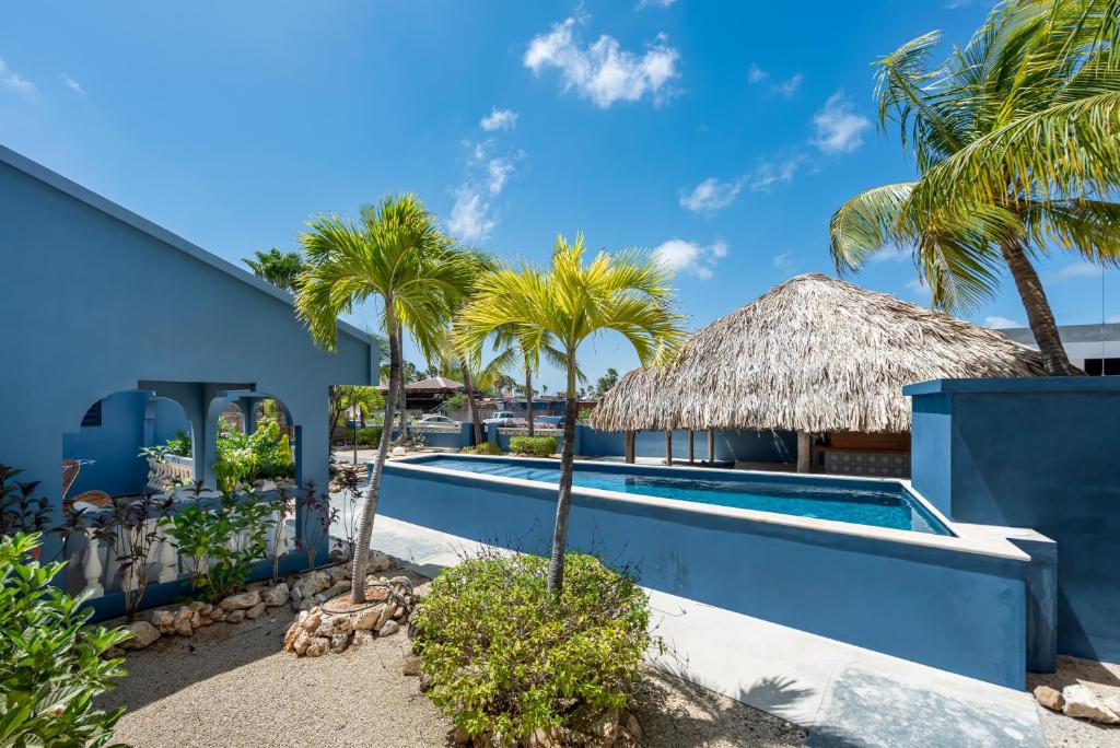 a resort pool with palm trees and a thatch roof at Blue Bonaire by Boutique Bonaire Unique Resorts in Kralendijk