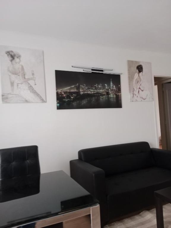 un salon avec un canapé noir et des tableaux au mur dans l'établissement Appartement à 10mn de paris, à Vitry-sur-Seine