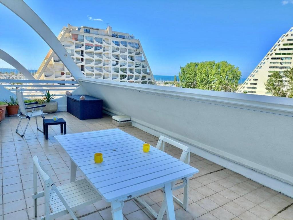 une table et des chaises blanches sur un balcon avec des bâtiments dans l'établissement Studio Lumineux avec Terrasse et Parking Privé, à 600m de la Plage - FR-1-716-76, à La Grande Motte