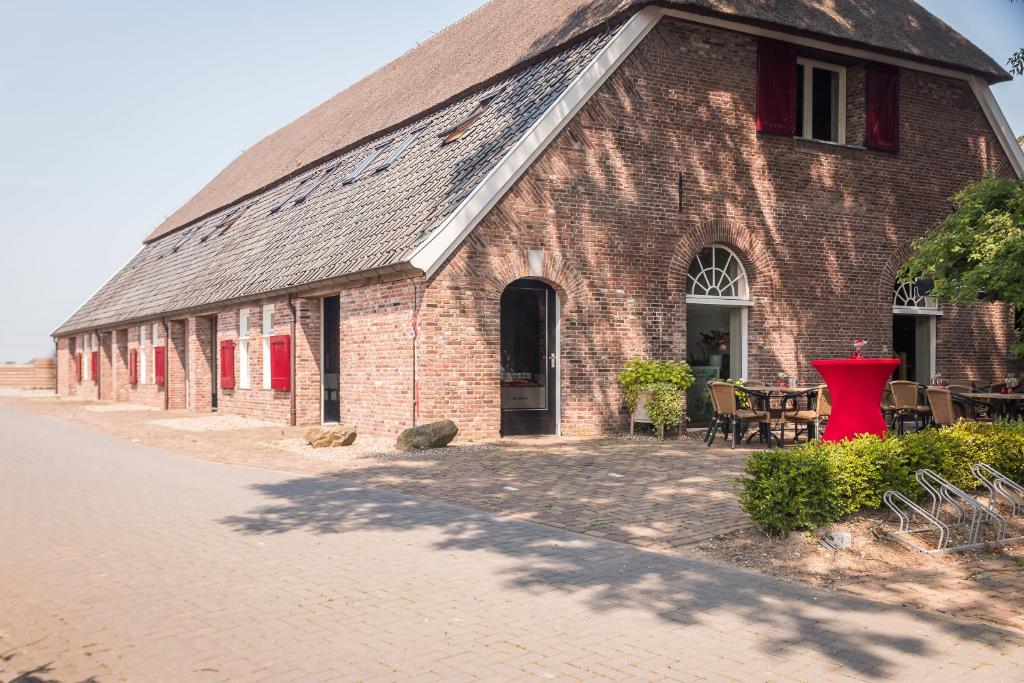 un edificio de ladrillo rojo con mesas y sillas delante de él en De Raayhof, en Pannerden