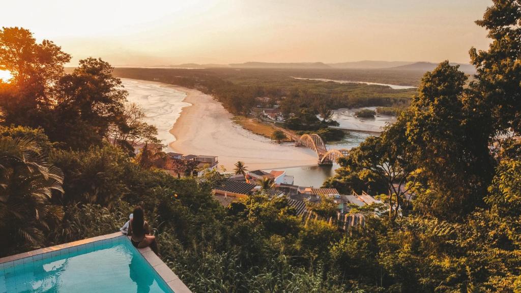 a woman standing on the edge of a swimming pool overlooking a beach at Banana Leaf Eco Hostel in Barra de Guaratiba