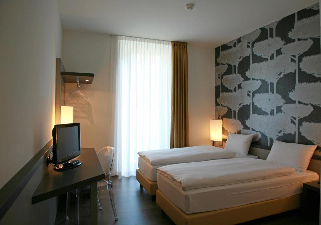 a hotel room with two beds and a desk with a television at Hotel Internazionale Bellinzona in Bellinzona