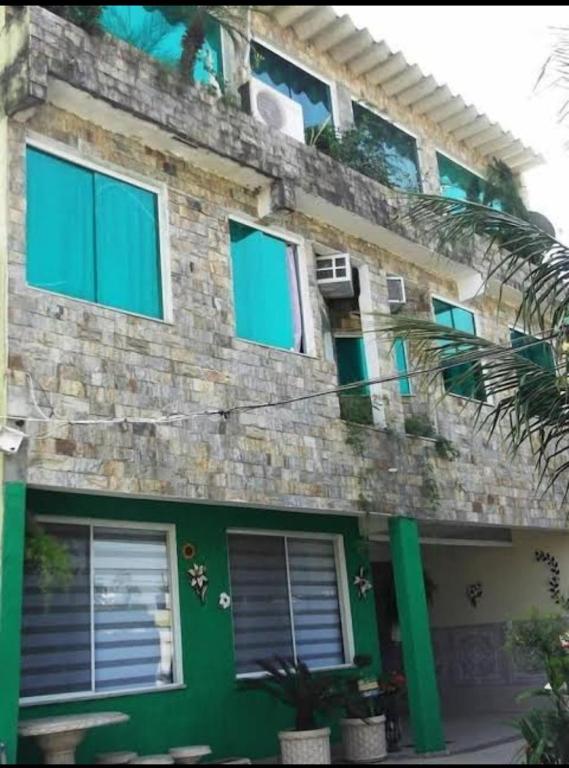 a green brick building with windows and a palm tree at Suítes felicidade Rio Centro in Rio de Janeiro