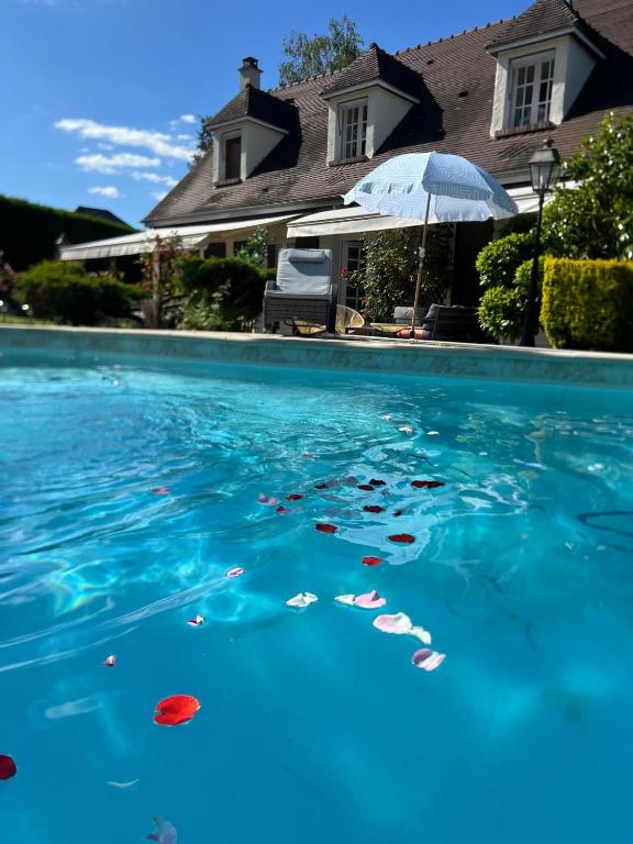 une piscine d'eau bleue avec un parasol et des sandicans dans l'établissement Villa proche Paris et Versailles, à Orgeval