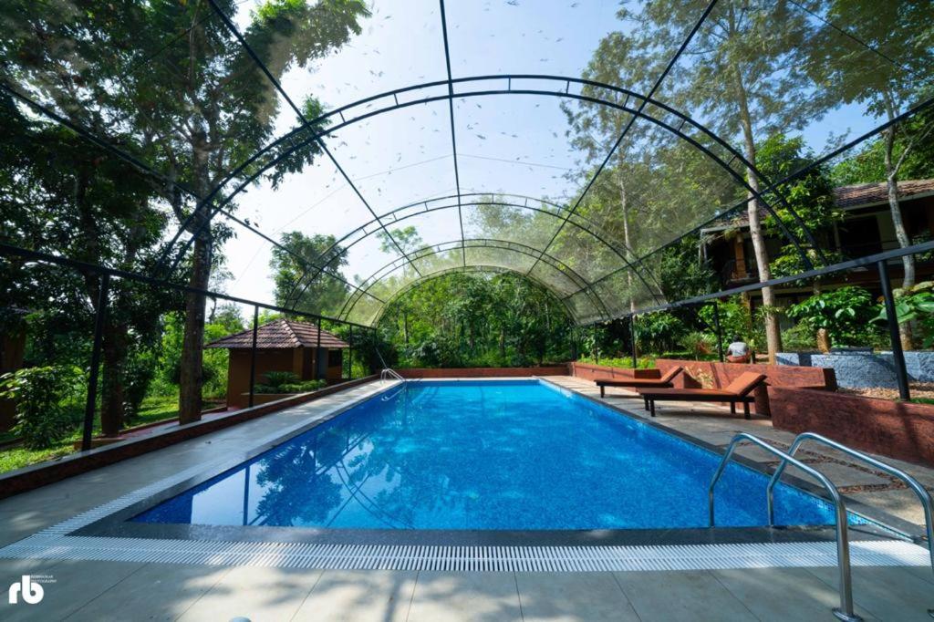 a swimming pool with a pergola over it at Wayanad Kuruva Isles Jungle Resort in Chekadi