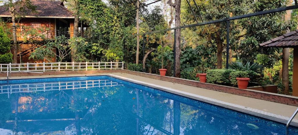 a swimming pool in front of a house with trees at Wayanad Kuruva Isles Jungle Resort in Chekadi