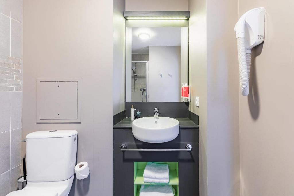 a bathroom with a sink and a toilet and a mirror at Appart’City Confort Le Bourget - Aéroport in Le Bourget