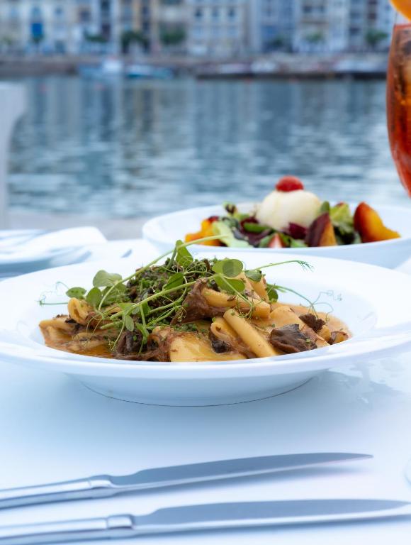 two plates of food on a table next to the water at Cavalieri Art Hotel in St. Julianʼs