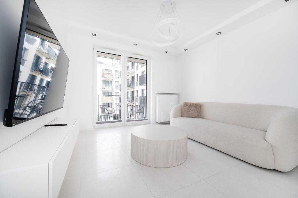 a white living room with a couch and a tv at Widzewska Deluxe Apartment by BookingHost in Łódź