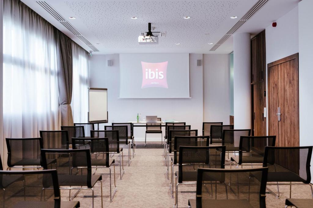 a lecture room with tables and chairs and a screen at Ibis Luxembourg Airport in Luxembourg
