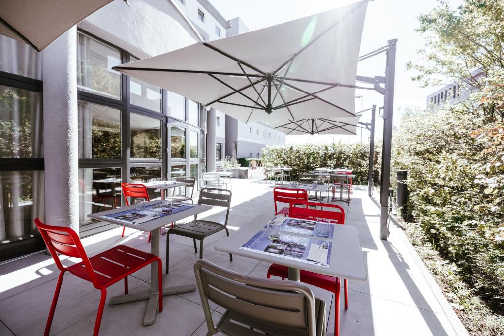 a patio with white tables and red chairs at Ibis Luxembourg Airport in Luxembourg