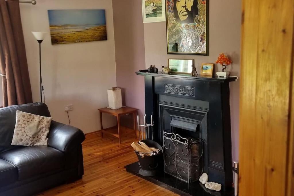 a living room with a black leather couch and a fireplace at ocean fields view in Ahnagh Cross