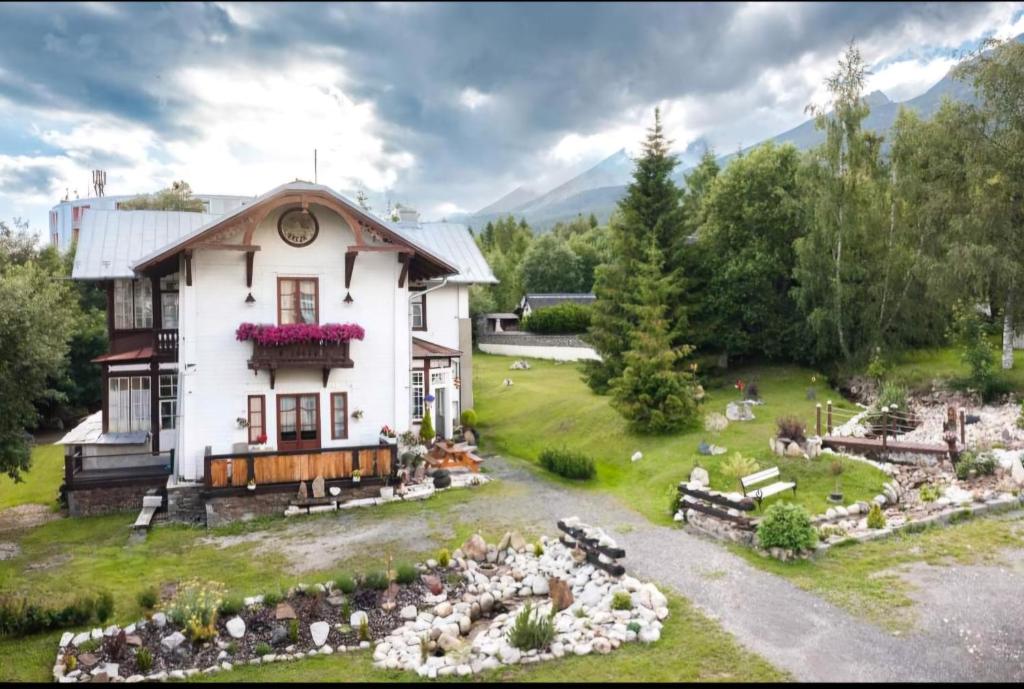 a large white house with a garden in front of it at Penzión Villa Breza in Smokovce