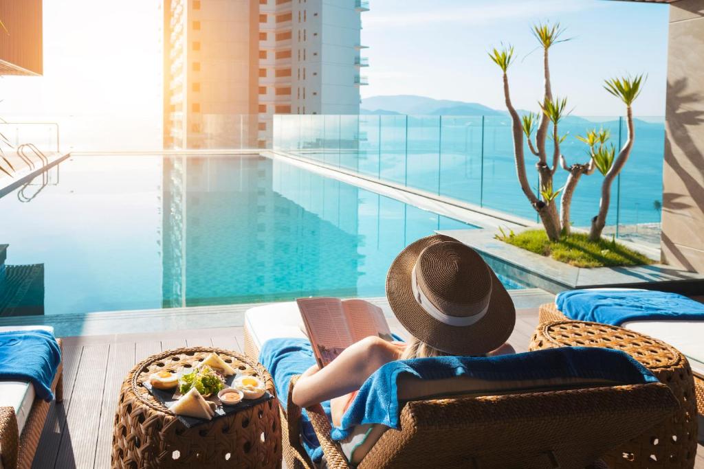 a woman in a hat sitting in a chair next to a swimming pool at Gonsala Hotel Nha Trang in Nha Trang