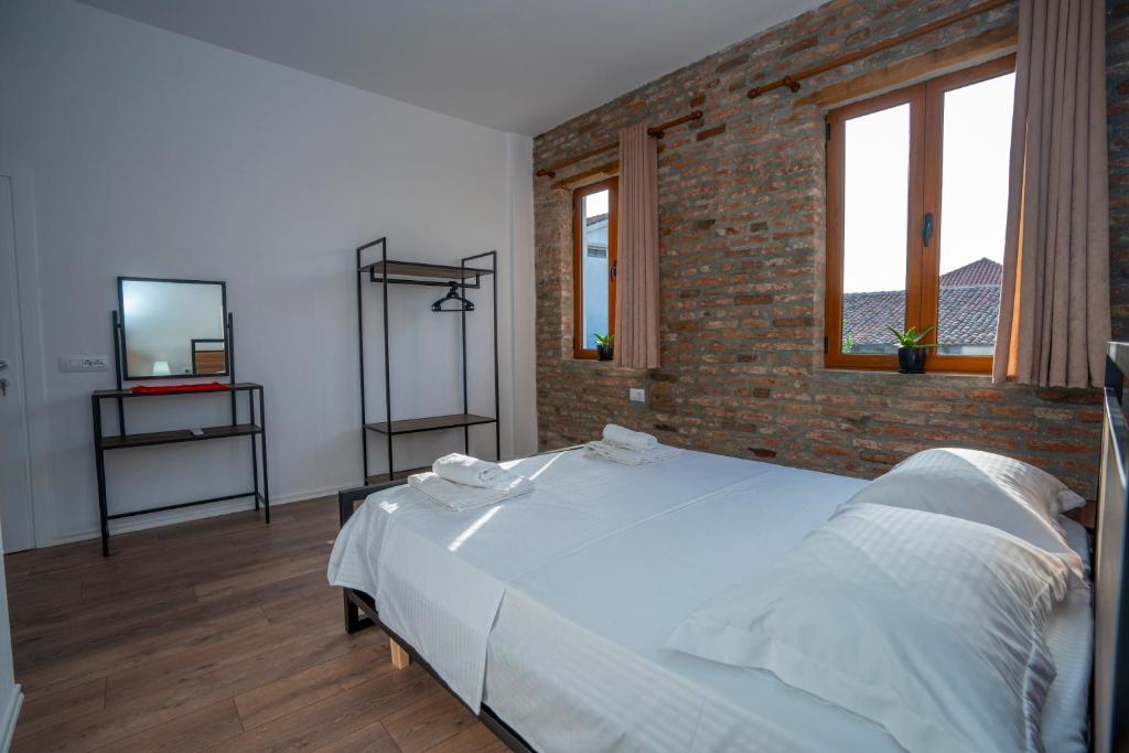 a bedroom with a large white bed with a brick wall at InTown Guesthouse Shkoder in Shkodër