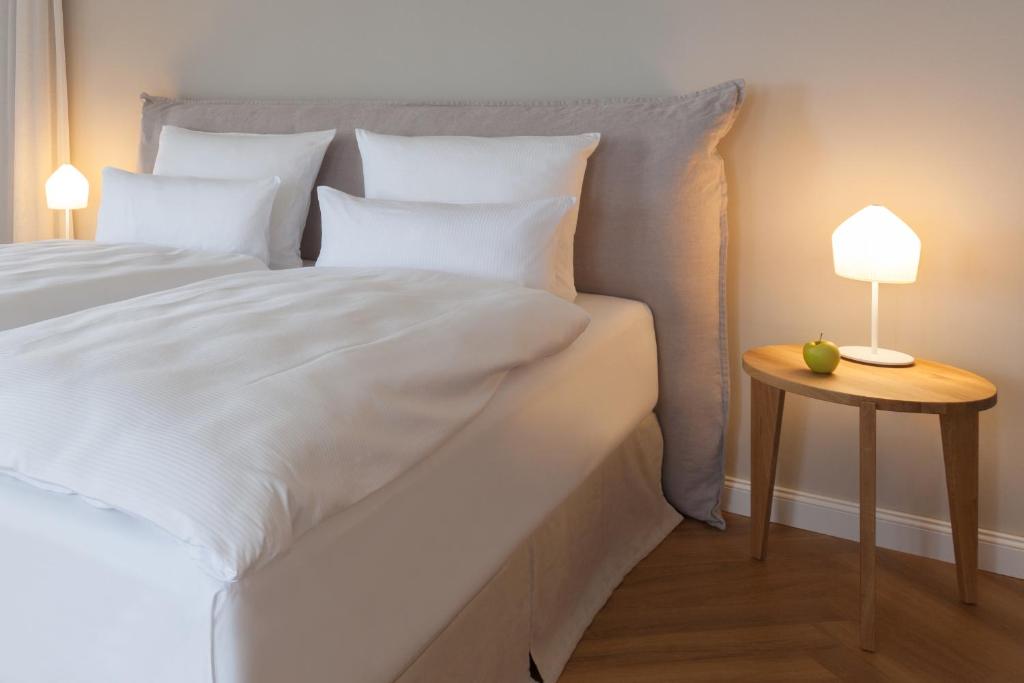 a white bed with white pillows and a side table at Vju Hotel Rügen in Göhren