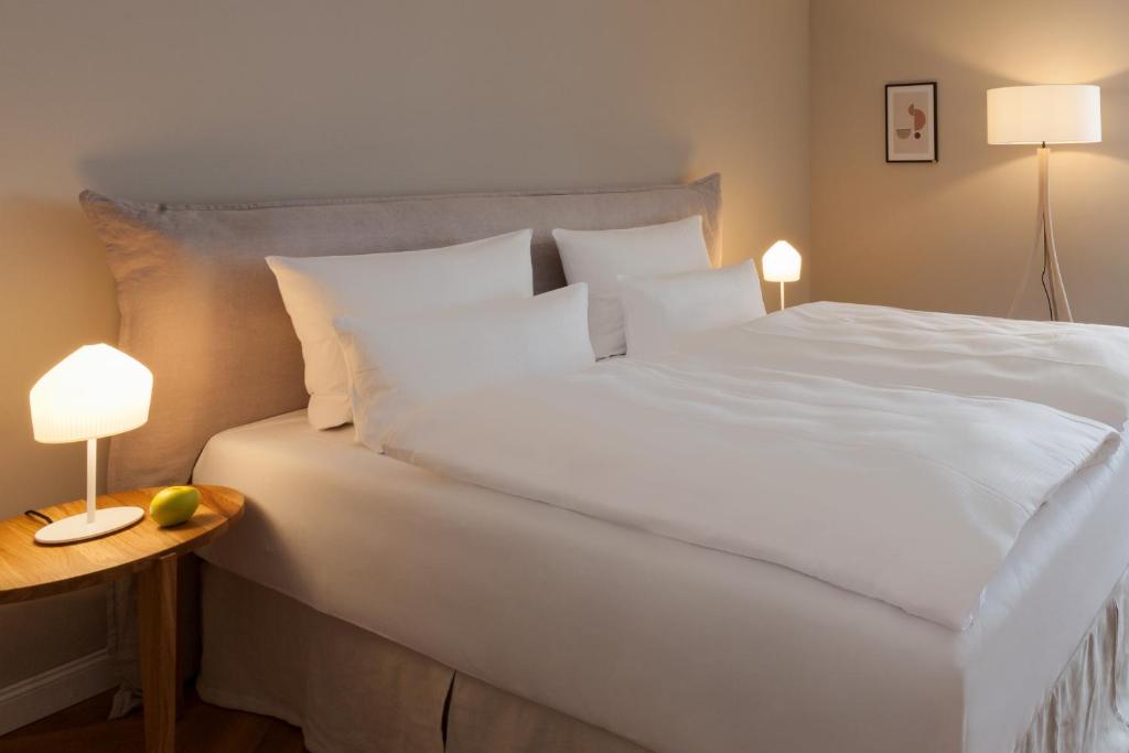 a large white bed with two lamps and a side table at Vju Hotel Rügen in Göhren