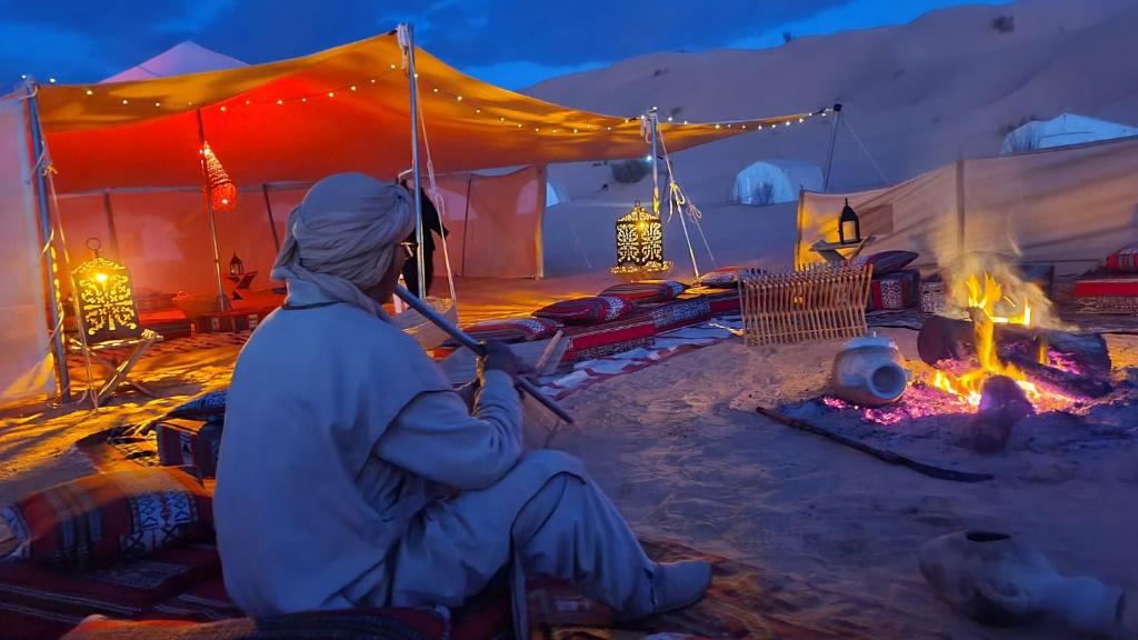 a person sitting in front of a tent with a fire at CAMP ABDELMOULA in Douz