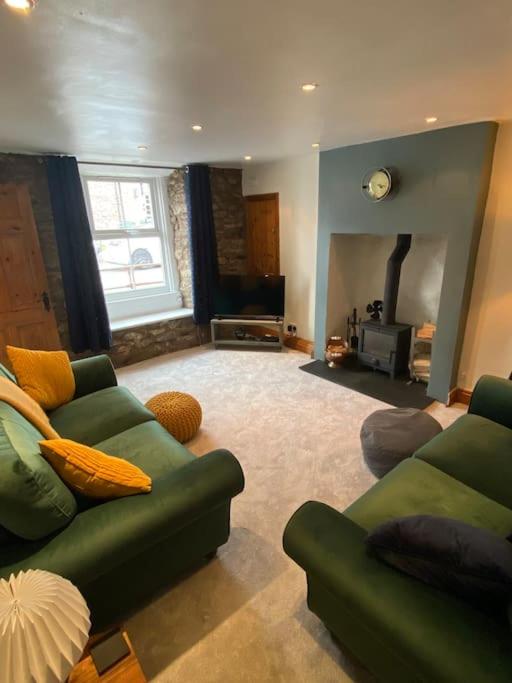 a living room with two green couches and a fireplace at Fettlers Cottage, Cumbria in Kirkby Stephen