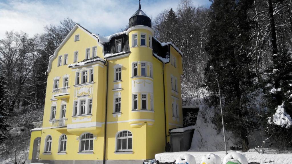 a yellow building with a black turret in the snow at Hotel Vera in Jáchymov
