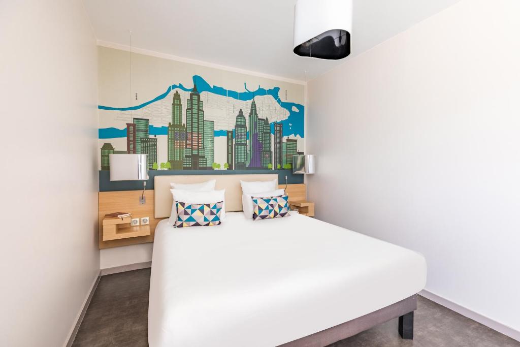 a bedroom with a white bed with a city mural on the wall at Appart’City Confort Lyon Cité Internationale in Caluire-et-Cuire
